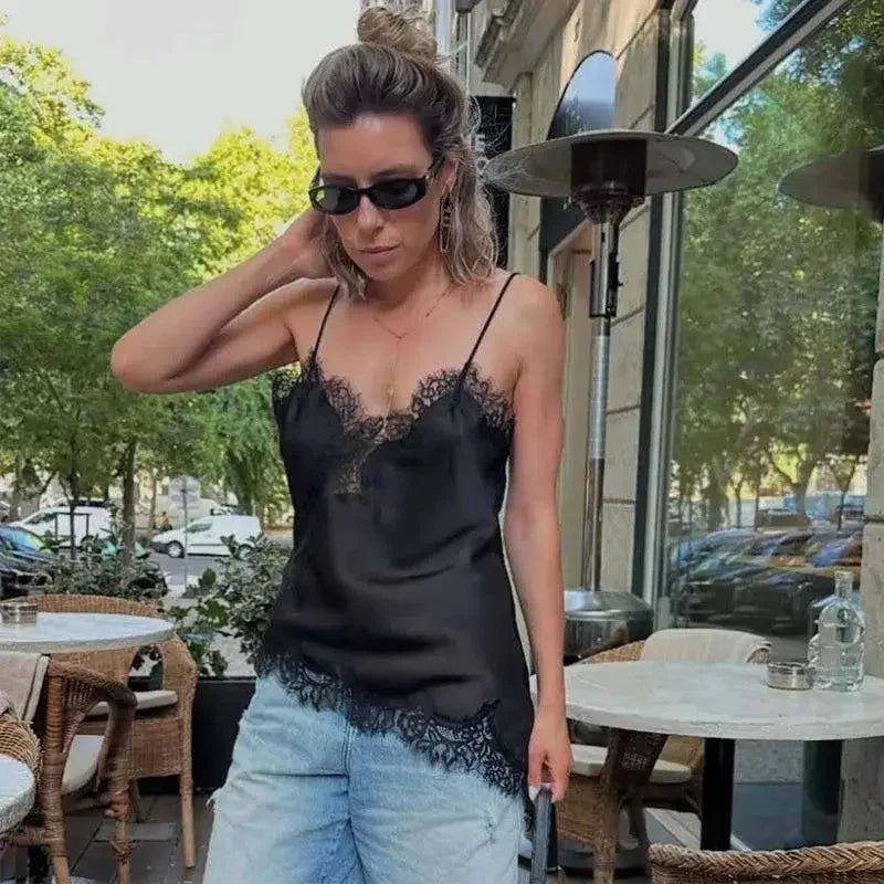 Woman in black lace camisole top and denim shorts at outdoor café, stylish summer fashion