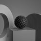 Black spiky massage ball on modern pedestal for muscle relief and wellness