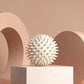 White spiky massage ball for muscle relief on minimalist pedestal, beauty and wellness accessory