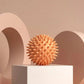 Spiky orange massage ball on white pedestal, minimalist beauty & wellness product display