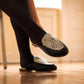 Black slip-on loafers with geometric pattern, worn with tights, stylish women's fashion footwear