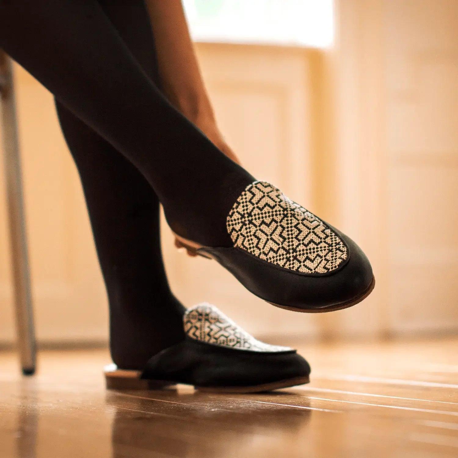 Black slip-on loafers with geometric pattern, worn with tights, stylish women's fashion footwear