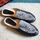 Black and white patterned women's slip-on loafers on textured rug, fashion footwear