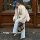 Woman in cozy cream faux fur coat, blue cap, light jeans, and sneakers with designer bag, street style fashion