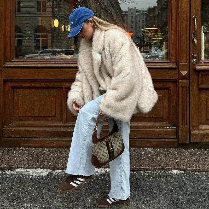 Woman in cozy cream faux fur coat, blue cap, light jeans, and sneakers with designer bag, street style fashion