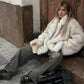 Woman in cozy white faux fur coat, olive jeans, and chunky boots holding coffee, urban street style fashion