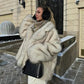 Woman in luxury faux fur coat, winter fashion, black earmuffs, stylish handbag, snowy outdoor setting