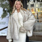 Woman in chic white faux fur coat and matching dress, carrying quilted handbag, stylish winter fashion