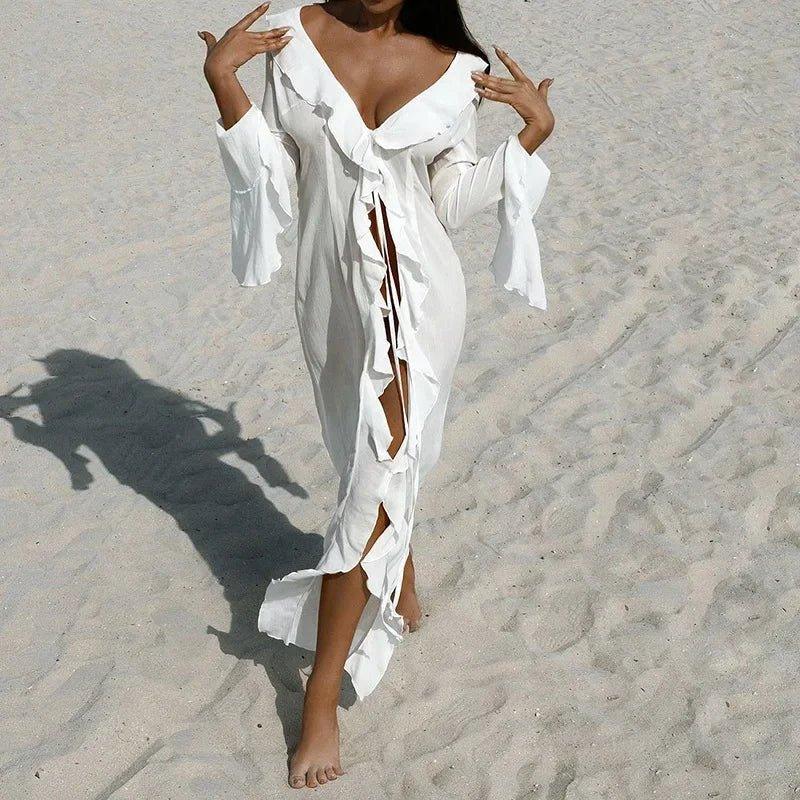 Woman in white beach cover-up dress with ruffles and slit, walking on sandy shore
