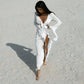 Woman in white ruffled beach cover-up dress walking on sandy shore