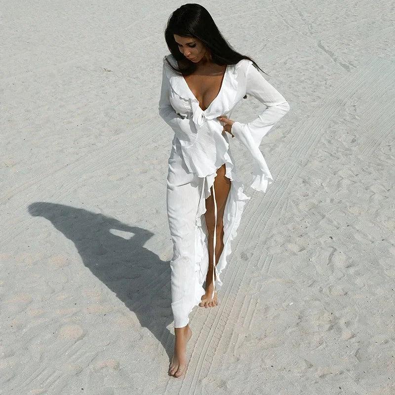 Woman in white ruffled beach cover-up dress walking on sandy shore