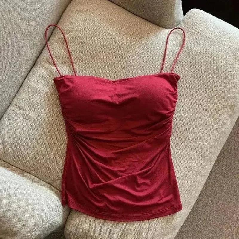 Red satin camisole top with thin straps, styled on beige sofa for women's fashion