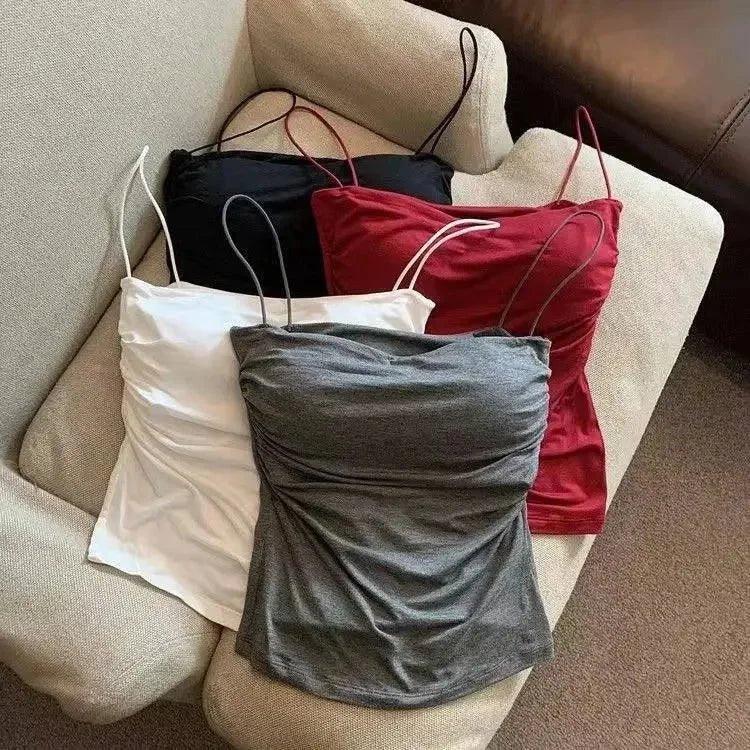 Women's ruched camisole tops in white, gray, red, and black, styled on a beige armchair for fashion display.