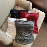 Women's ruched camisole tops in white, gray, red, and black, styled on a beige armchair for fashion display.