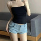 Woman in black spaghetti strap top and light denim shorts, casual summer fashion