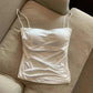White satin camisole top with ruched front and thin straps, laid on beige sofa
