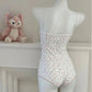White floral one-piece bodysuit with thin straps, displayed on mannequin beside plush toy