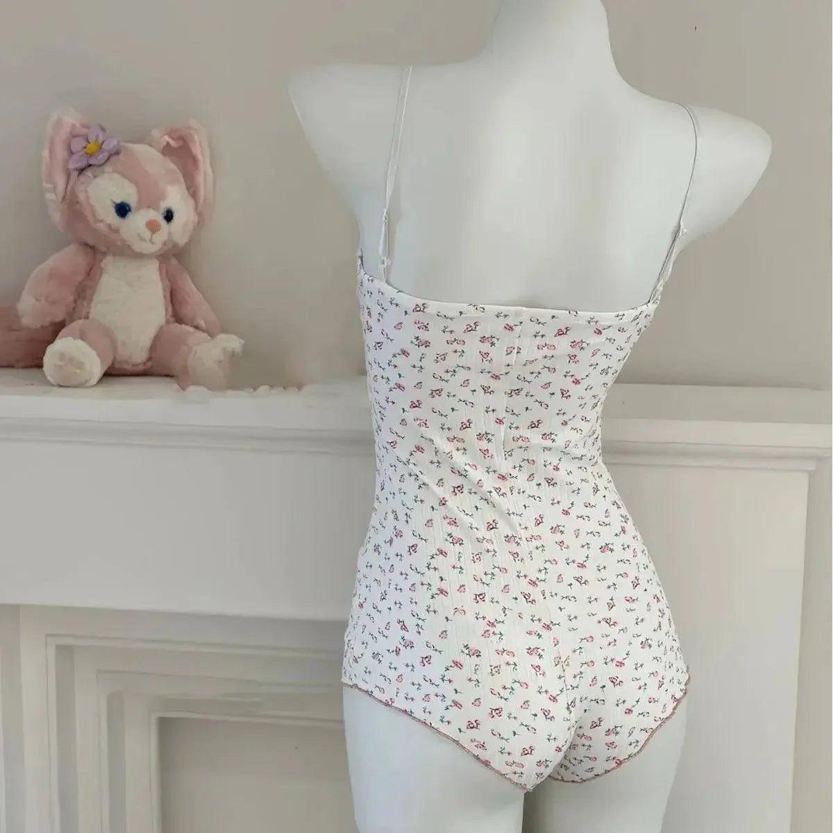 White floral one-piece bodysuit with thin straps, displayed on mannequin beside plush toy