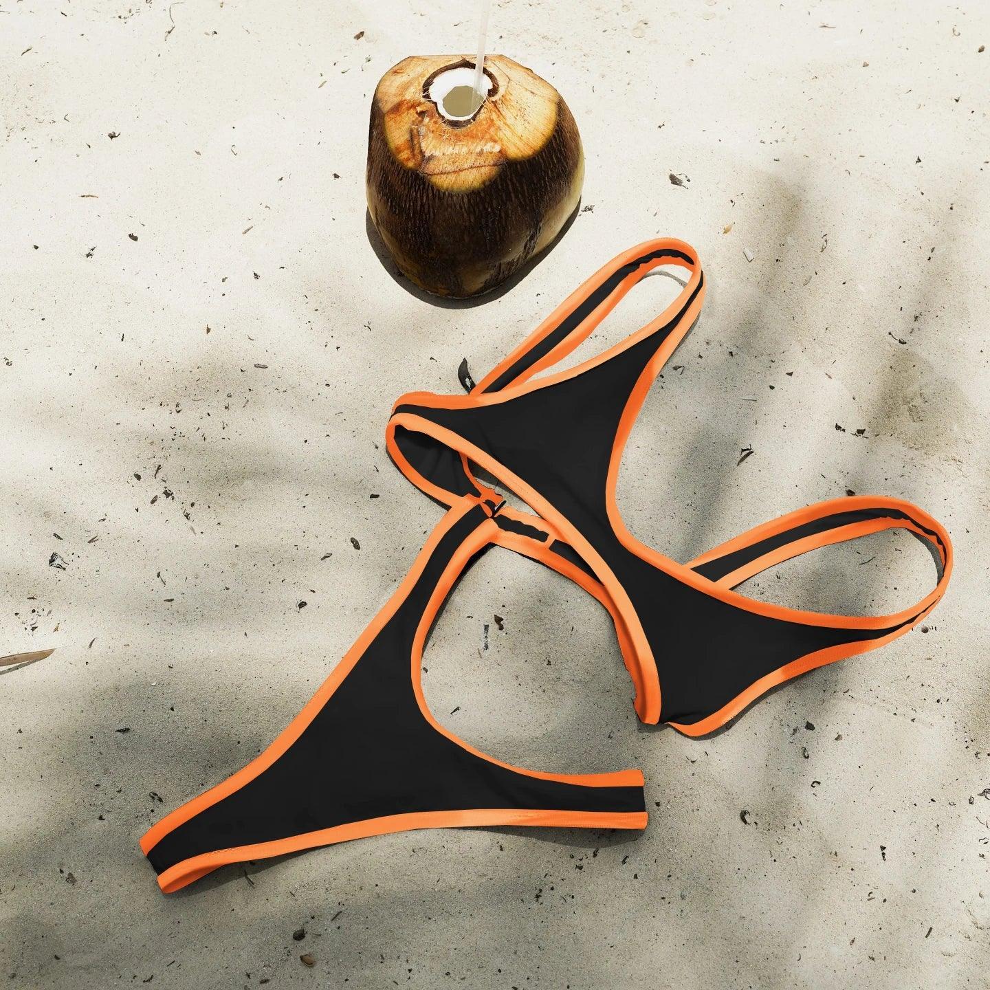 Black and orange bikini set on sandy beach with fresh coconut, perfect for summer fashion