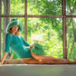 Woman in teal swimsuit with green knit hat and bag, posing by window with lush greenery outside