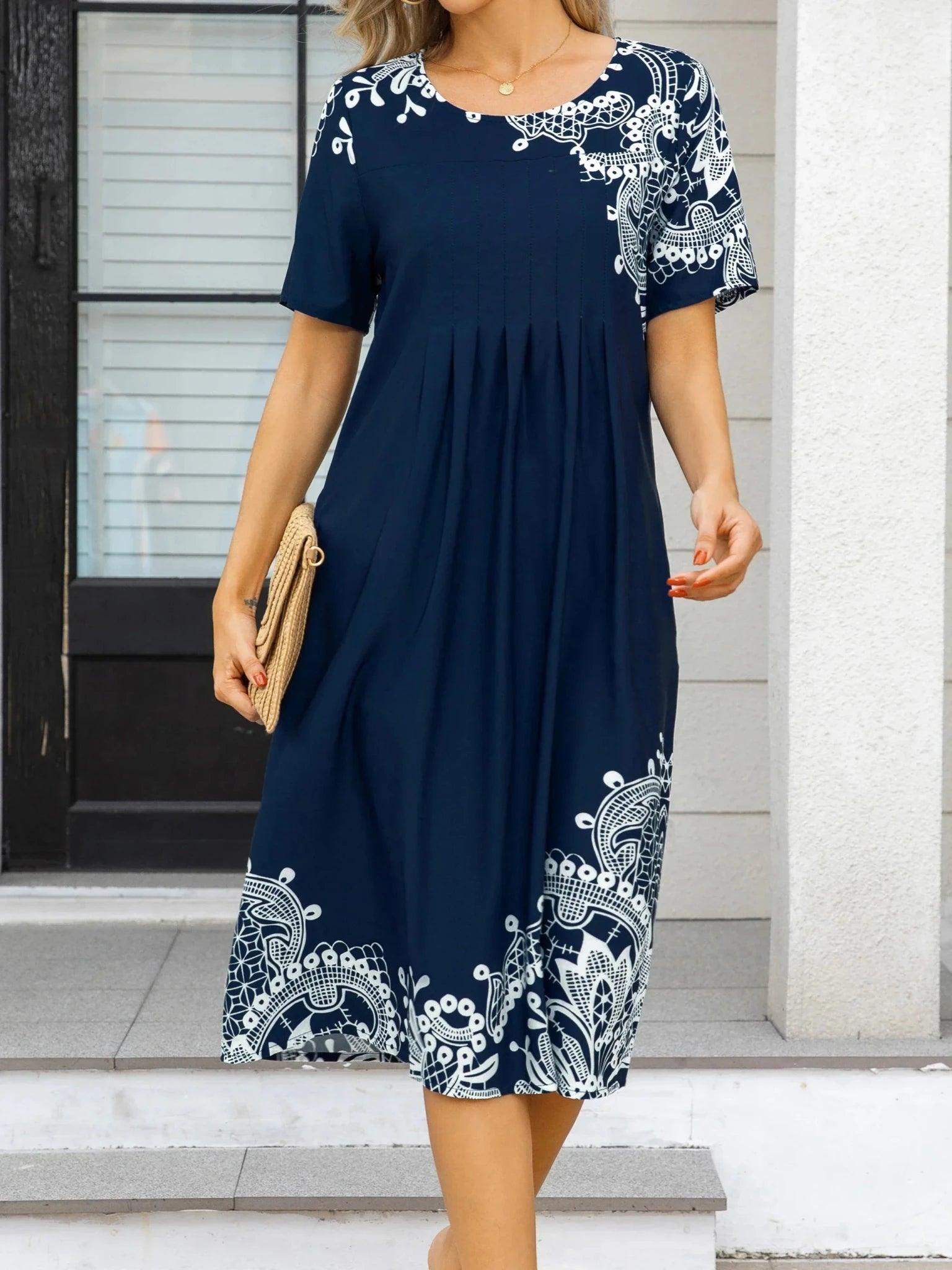 Navy blue women's midi dress with white lace print, short sleeves, and pleated waist, styled with straw clutch