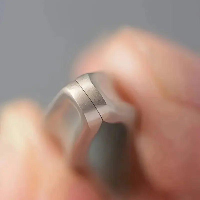 Minimalist silver ring with geometric facets, held between fingers for close-up detail