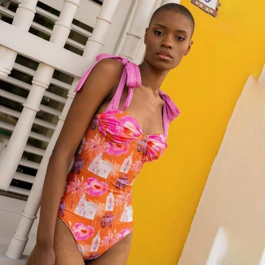 Woman in vibrant orange floral one-piece swimsuit with pink tie straps, stylish beachwear fashion