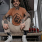Man with tattoos wearing 'Raise Hell Eat Tacos' graphic tee, beige pants, and white sneakers on stairs