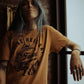 Woman wearing mustard graphic tee with 'Raise Hell Eat Tacos' print, tattoos, rings, and chain necklace