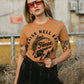 Woman wearing 'Raise Hell Eat Tacos' graphic tee, sunglasses, and black jeans, edgy street style fashion