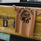 Tan graphic tee with 'Raise Hell Eat Tacos' design draped on vintage yellow truck tailgate