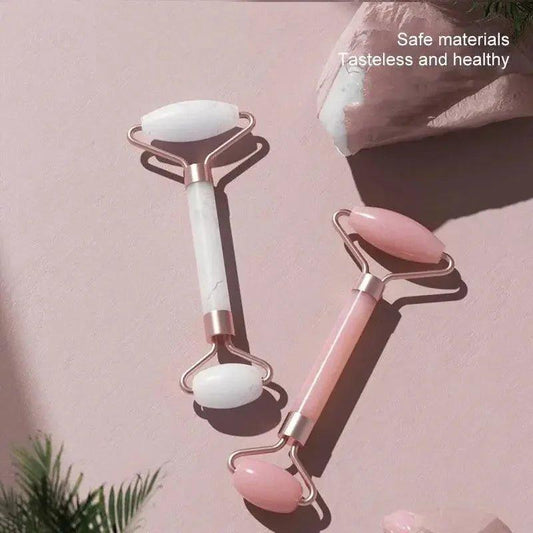 Pink and white jade facial rollers for skincare, beauty tools with rose gold handles on soft pink background