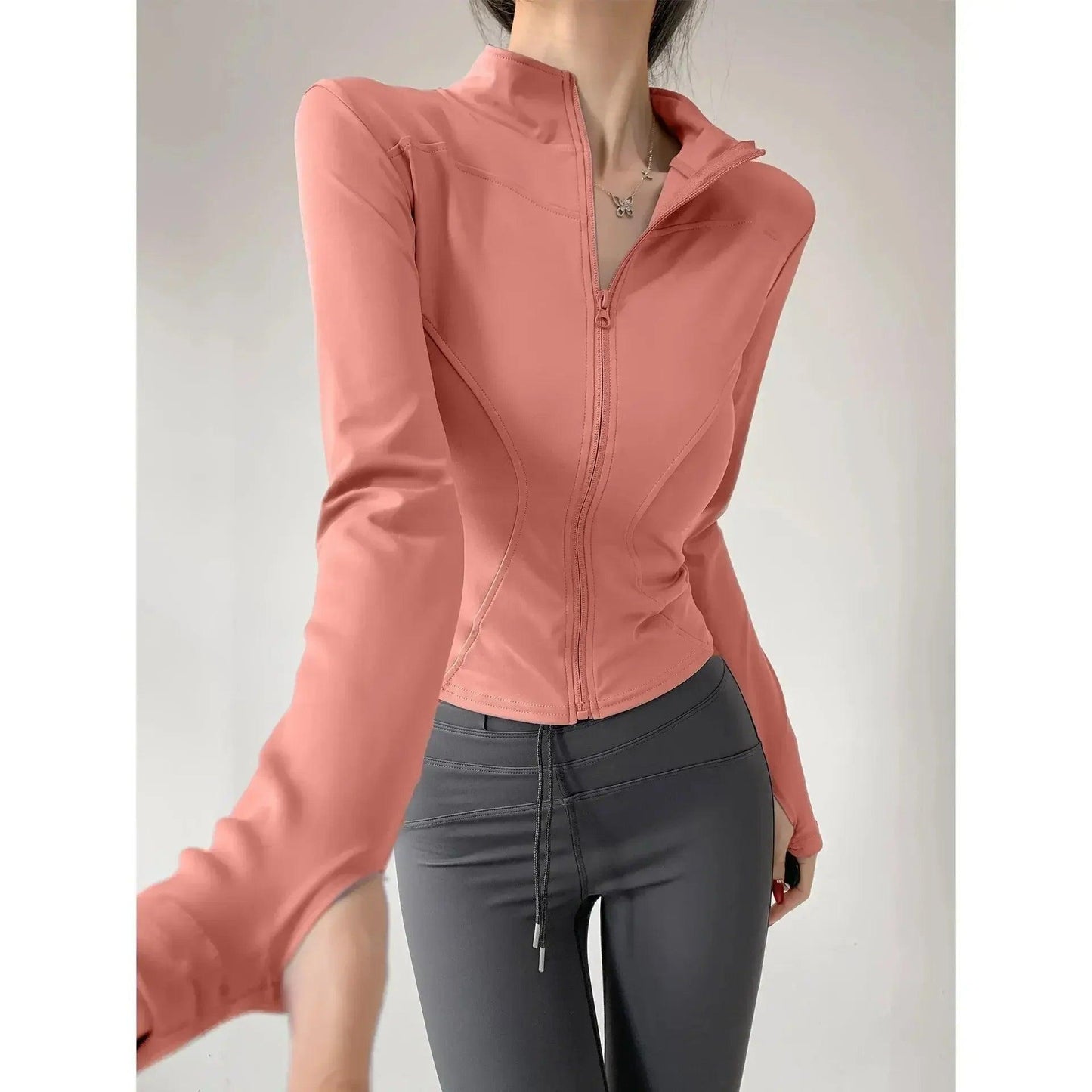 Pink zip-up women's fitness jacket with long sleeves, paired with gray leggings for workout or casual wear.