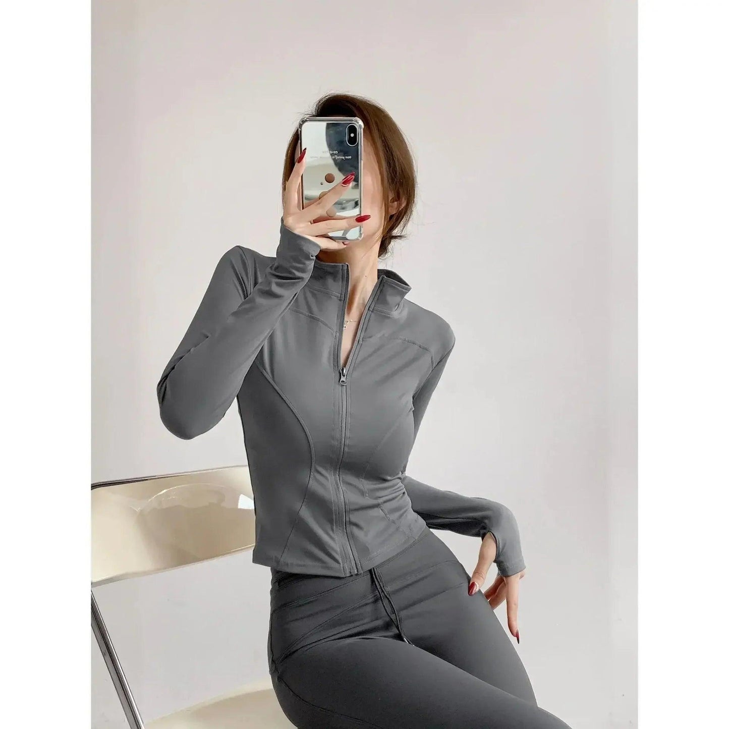 Woman in gray zip-up long sleeve activewear top and matching leggings, taking mirror selfie