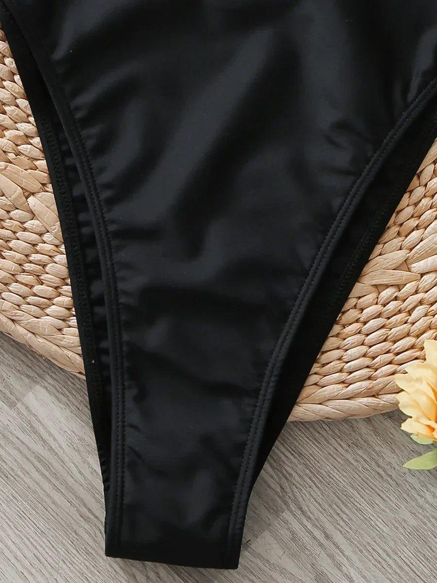 Black high-cut bikini bottom on woven mat with yellow flower, women's swimwear fashion