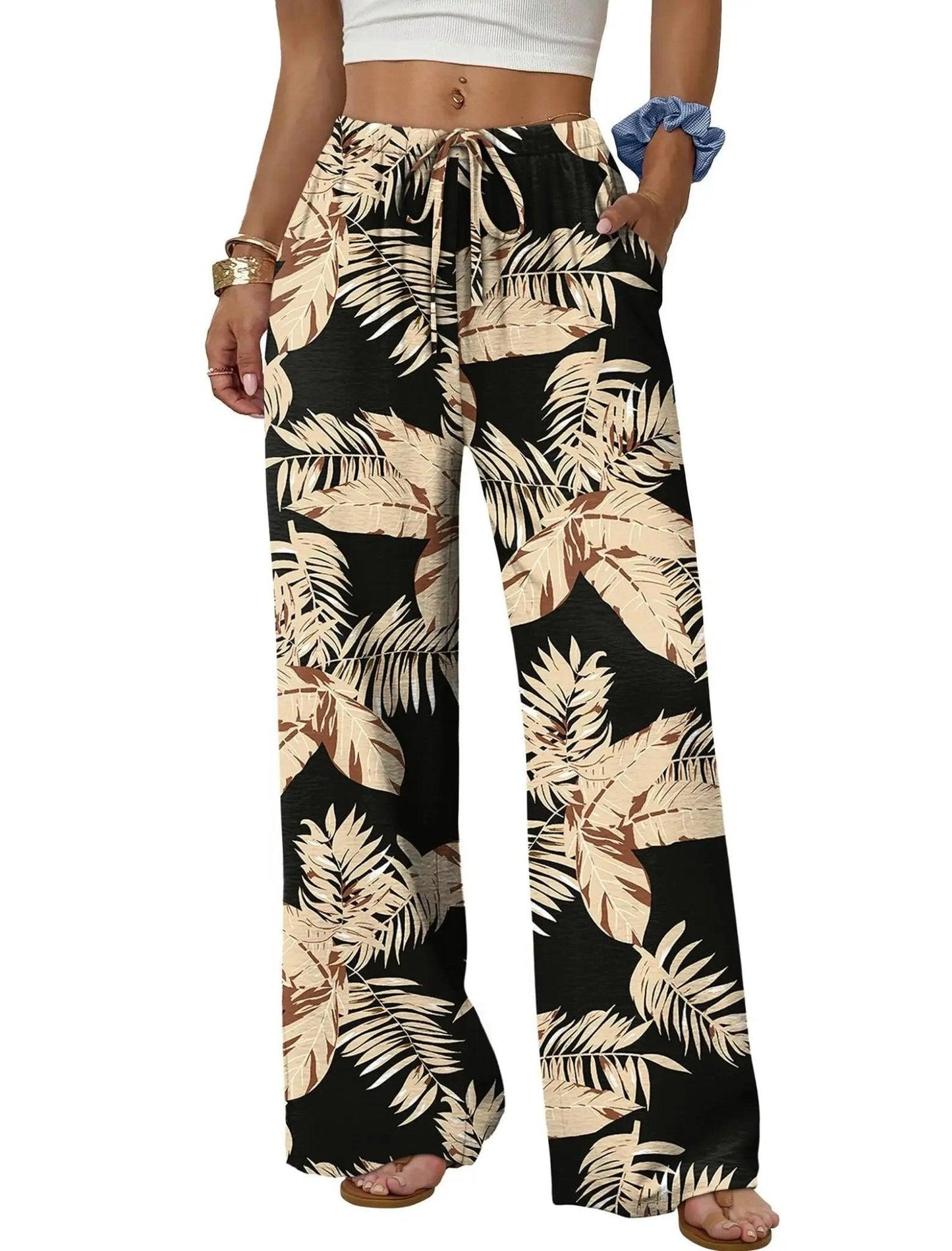 Women's tropical leaf print wide-leg pants with drawstring waist, paired with white crop top and sandals