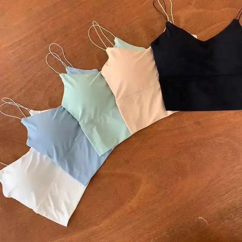 Women's spaghetti strap camisoles in white, blue, mint, pink, and black on wood