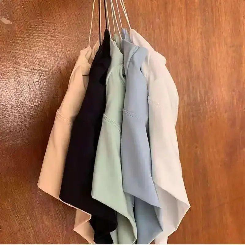 Women's fashion tops in pastel and neutral colors hanging on hangers against wooden background
