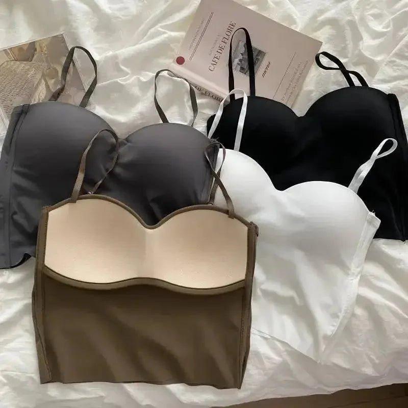 Women's seamless bras in black, white, gray, and beige, styled on white bedding with fashion magazine