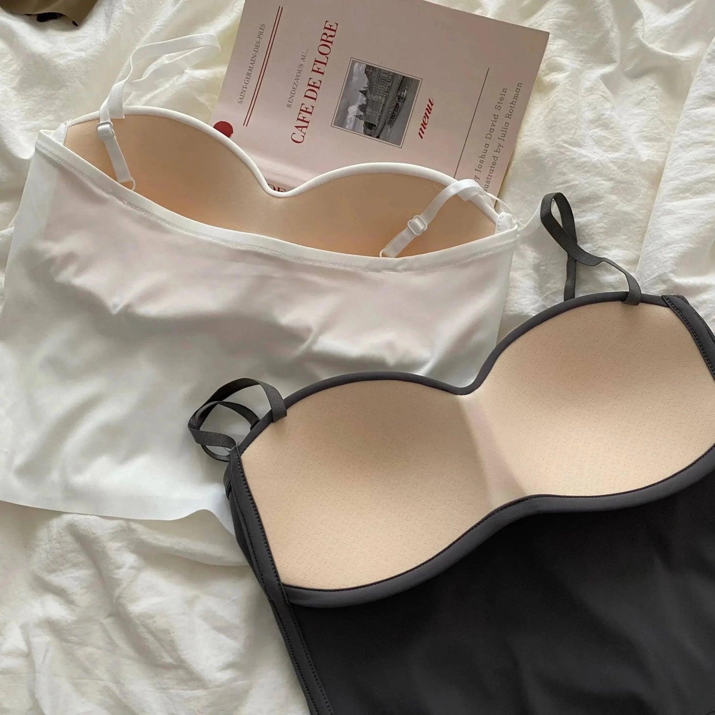 White and black women's camisole tops with adjustable straps, styled on bed with book for fashion look