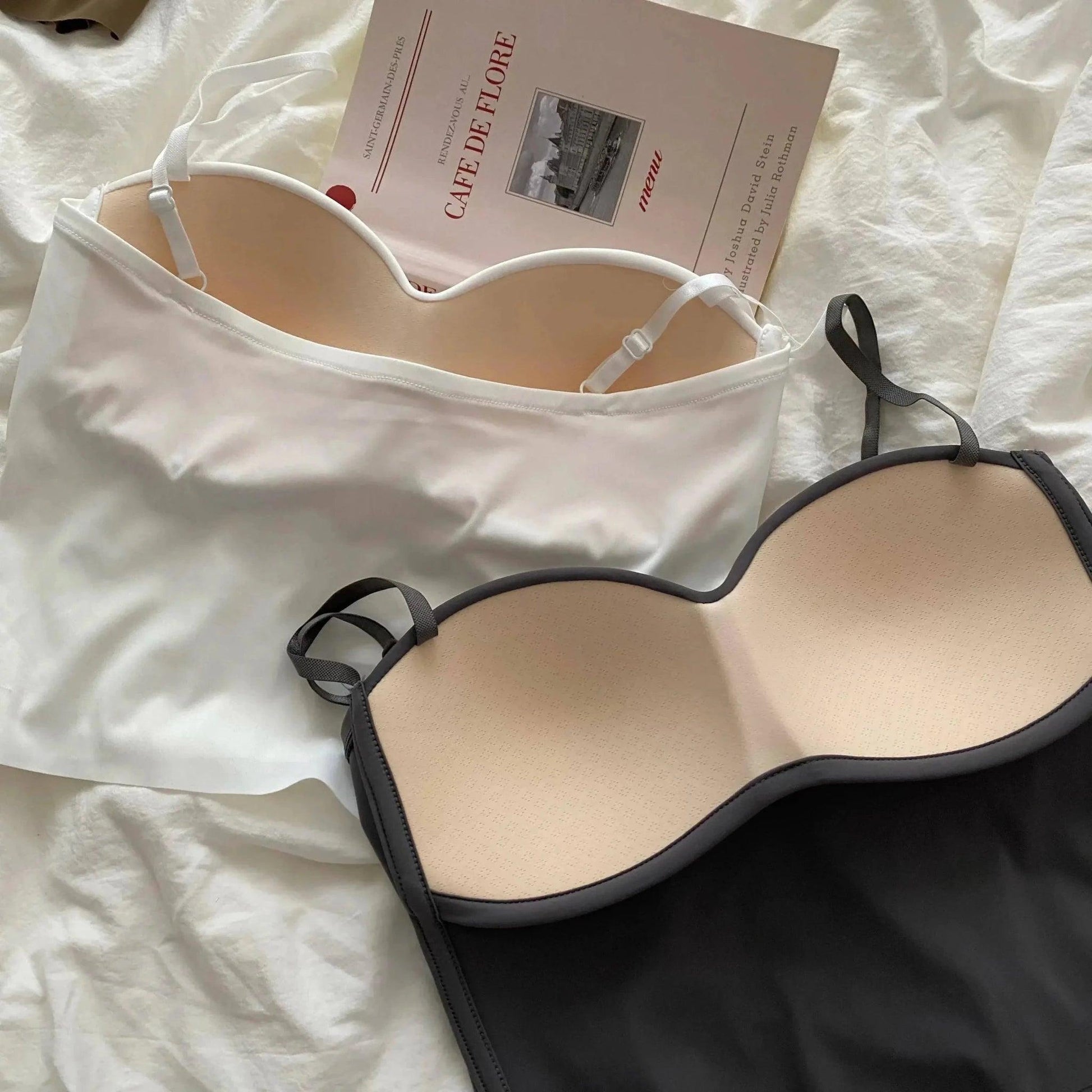 White and black women's camisole tops with adjustable straps, styled on bed with book for fashion look