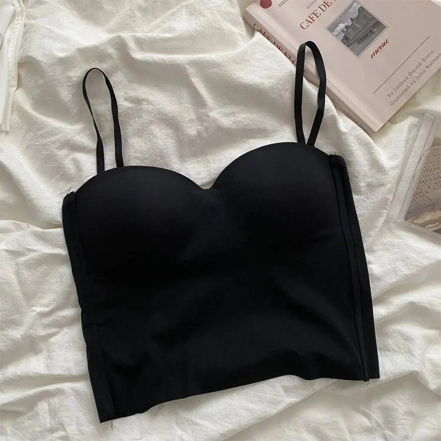 Black strapless bralette with thin straps, laid on white fabric beside a book, women's fashion