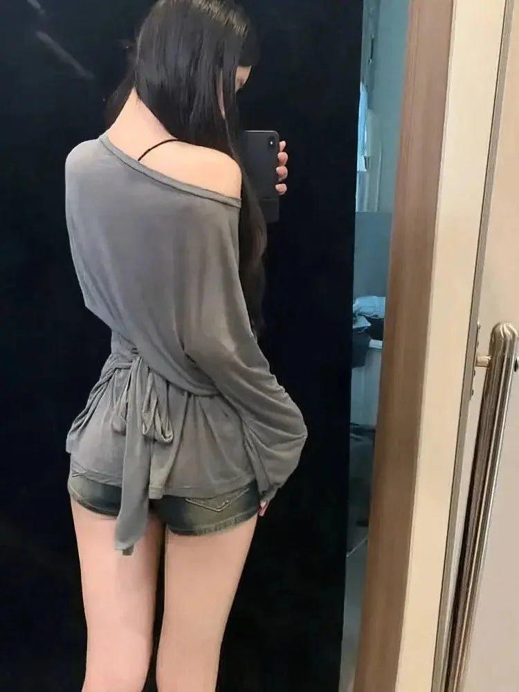 Woman taking mirror selfie in gray off-shoulder top and denim shorts, casual fashion outfit