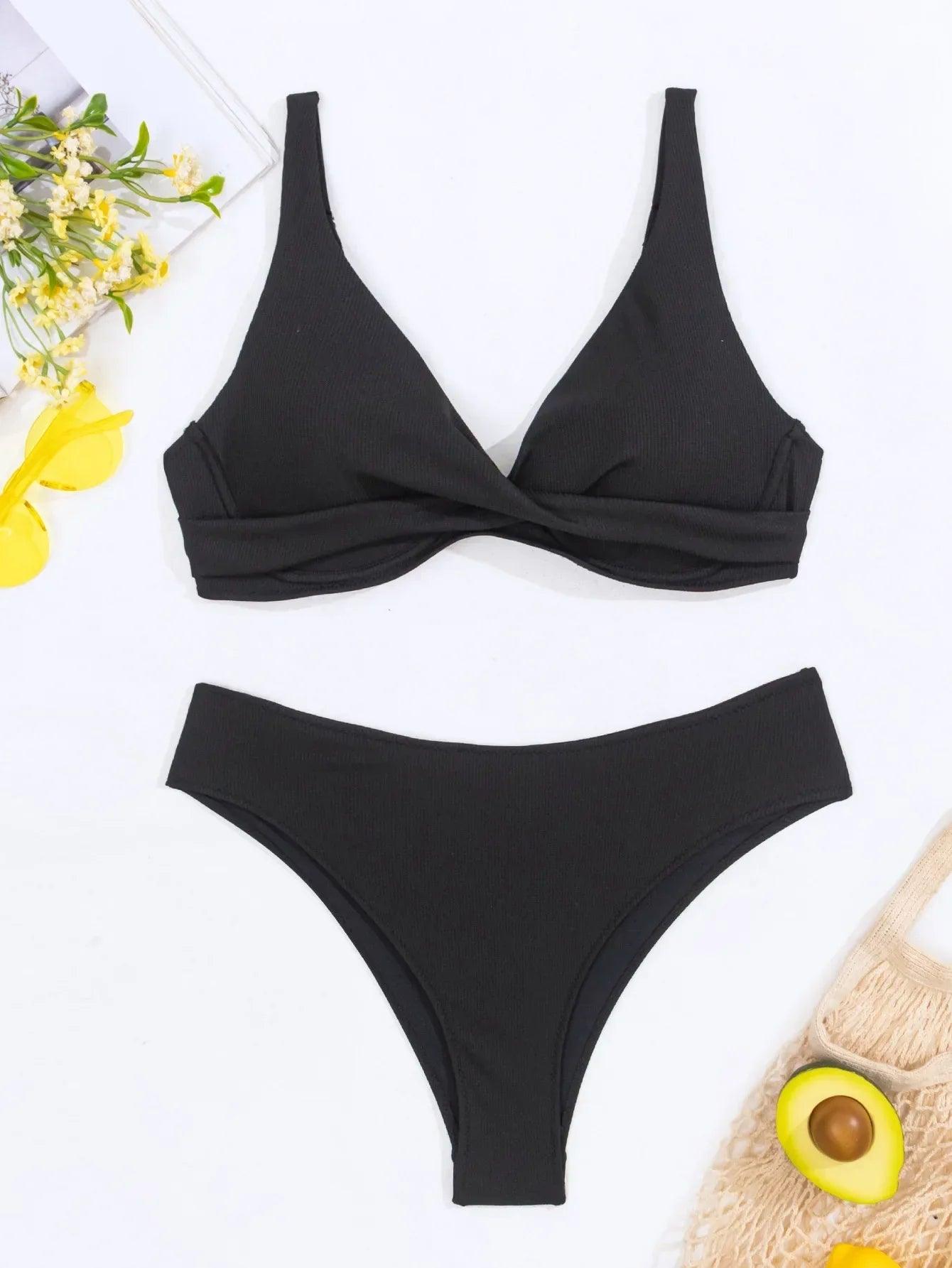 Black ribbed bikini set with twist front top and high-cut bottoms, styled with yellow flowers and avocado