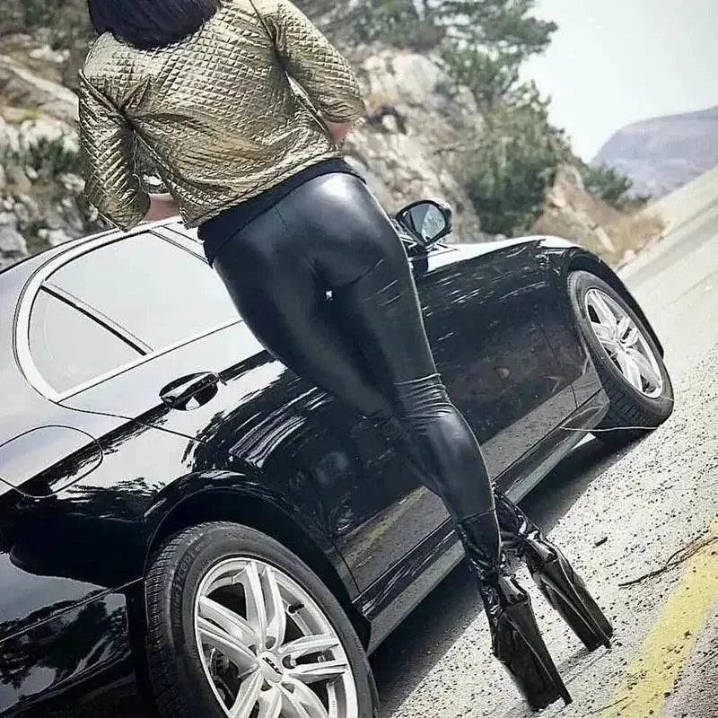 Woman in gold quilted jacket and black leather leggings posing by luxury car on mountain road