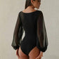 Woman in black bodysuit with sheer long sleeves, back view, fashion wear