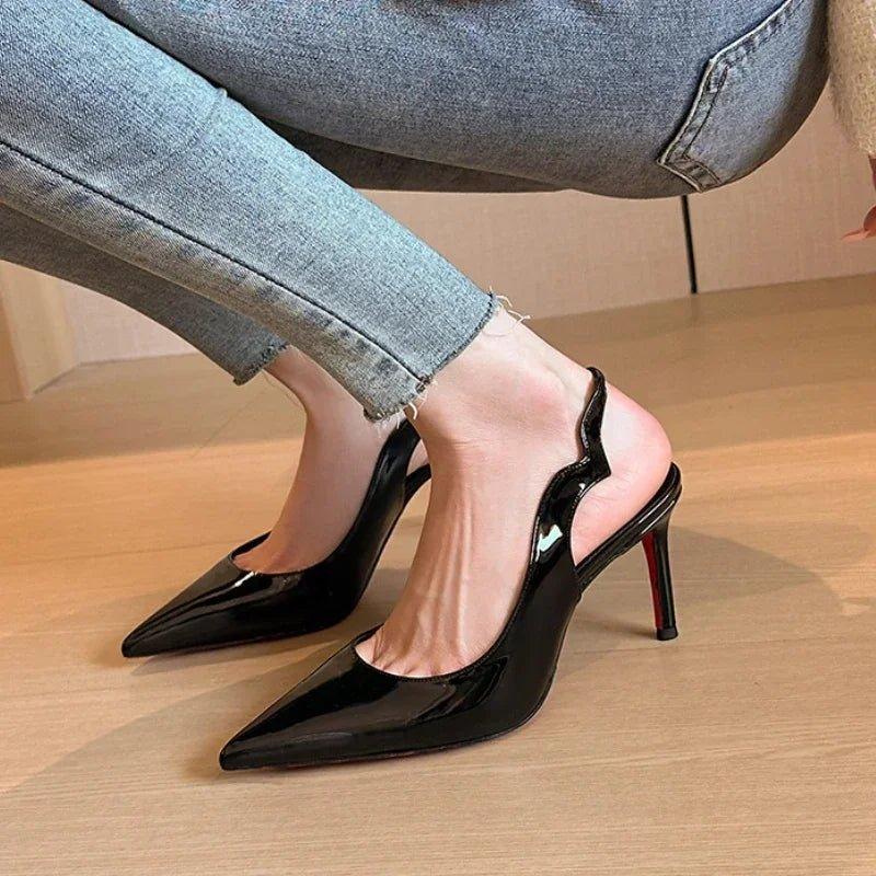 Black patent leather pointed-toe high heels with slingback design, paired with light denim jeans