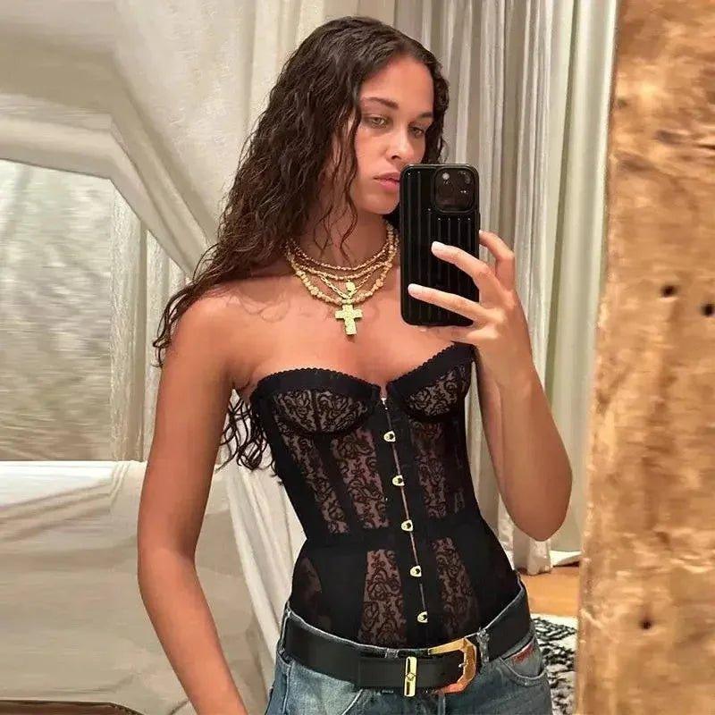 Woman in black lace corset top with gold buttons, layered necklaces, and jeans, taking mirror selfie