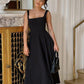 Woman in elegant black midi dress with square neckline, holding braided handbag, luxury fashion