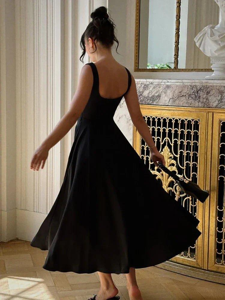 Woman in elegant black midi dress with open back, twirling in luxury interior